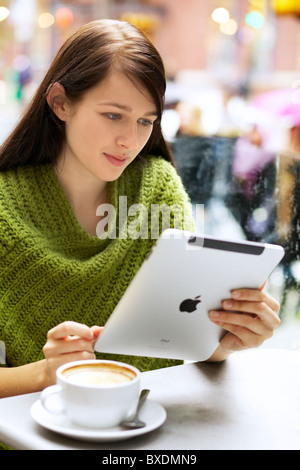 Young woman relaxing with her cappuccino tout en naviguant sur son iPad avec piscine Banque D'Images