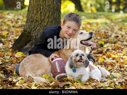 Smiling Young boy posant devant l'appareil photo avec son Goldren Retriever et Shih Tzu et son ballon de rugby Banque D'Images