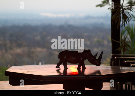 Les captures de rhino en bois sculpté les derniers rayons rouges du soleil sur une table à l'entrée de Stanley Safari Lodge, près de Livingstone, Zambie Banque D'Images
