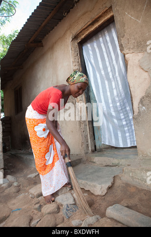 Une jeune femme balaie son porche à Dodoma, Tanzanie, Afrique de l'Est. Banque D'Images