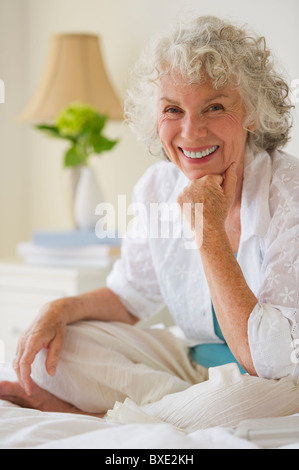 Portrait d'une femme aux cheveux gris sitting on bed Banque D'Images
