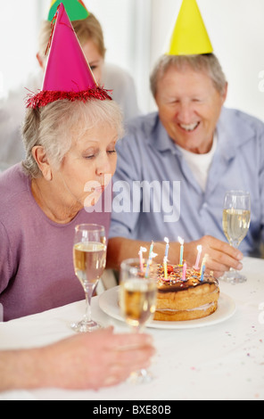 Senior woman blowing out les bougies sur un gâteau d'anniversaire Banque D'Images