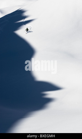 Un skieur de télémark de prendre un virage en poudre en Disentis, Suisse. Les montagnes ont jeté une ombre qui ressemble à un profil d'homme. Banque D'Images