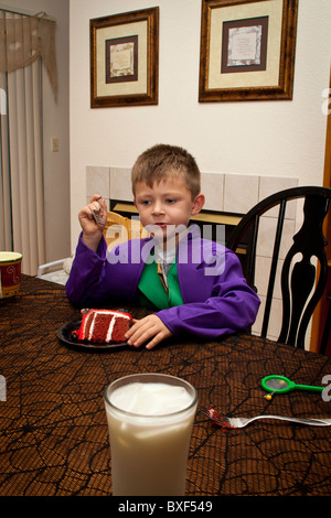 Un jeune garçon manger un gâteau et de boire du lait dans son costume Halloween Banque D'Images