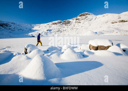 L'alpiniste marche sur la glace sur Easedale Tarn au-dessus de Grasmere dans le Lake District, UK, gelé par une vague de froid en décembre 2010. Banque D'Images