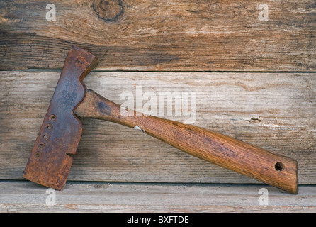 Ancien outil de hache pour marteau de bardeaux en fer reposant sur une ancienne étagère en bois. Banque D'Images