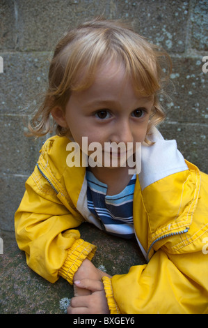 Petit, large-eyed girl portant un imperméable jaune, Provence, France. Banque D'Images