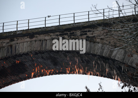 Les glaçons, allume en rouge par le soleil couchant, s'accrocher à partir de l'une des arches du viaduc de Victoria à Washington, England, UK Banque D'Images