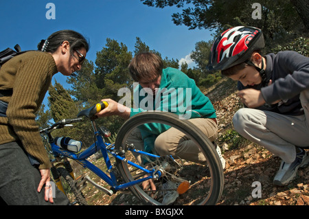 Les parents s'arrêter pour aider leur fils réparer le pneu de son vélo de montagne. Banque D'Images