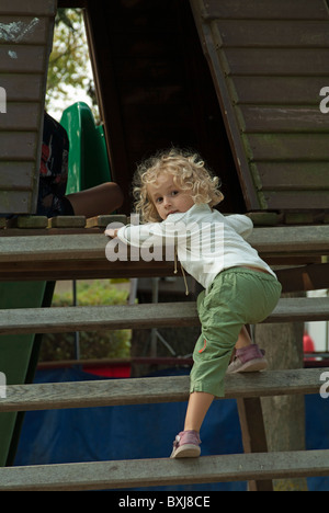 Fillette de trois ans l'escalade des marches de bois dans l'aire d'un parc public. Banque D'Images