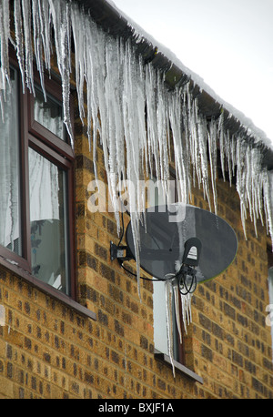 Beaucoup de gros glaçons pendant d'une gouttière de toit et une antenne parabolique. UK, décembre 2010. Banque D'Images