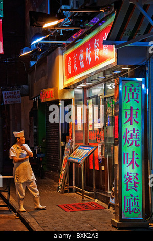 Cuisine asiatique travailleur masculin debout à l'extérieur du restaurant fumer une cigarette dans le centre-ville de Hong Kong, Chine Banque D'Images