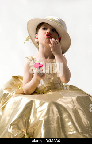 Isolated on white sweet brunette petite fille en robe de lumière dorée et white hat qui composent ses lèvres Banque D'Images