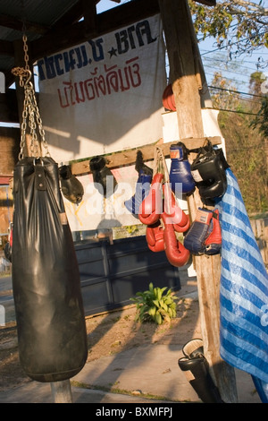 Rouge, noir et bleu gants de boxe Muay Thai, avec support de sac, sont en face d'une salle de sport en milieu rural dans la région de Mae Sariang, Thaïlande. Banque D'Images