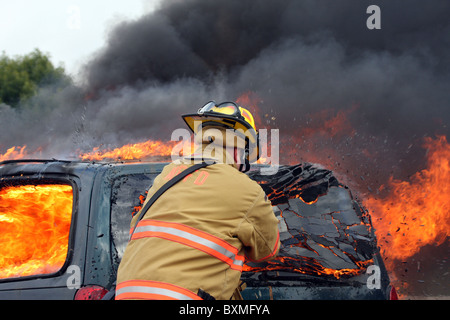 Un pompier casser la fenêtre arrière d'une voiture en feu Banque D'Images