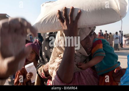 Le Pakistan, dans la province du Sind, Shaddat Kot .Après l'inondation. Décembre 2010. Une femme porte son accueil sac de farine de blé. Banque D'Images