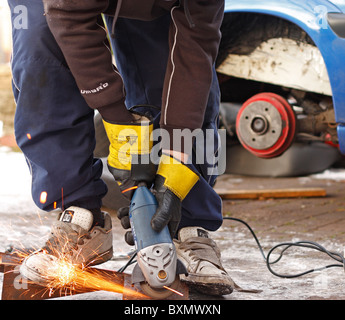 Un jeune homme à l'aide d'une meuleuse d'angle tout en travaillant sur la réparation du châssis d'une voiture, le port de gants de protection. Banque D'Images