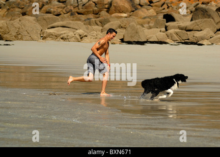 Man chasing son chien sur la plage de Sennen, Cornwall. Banque D'Images