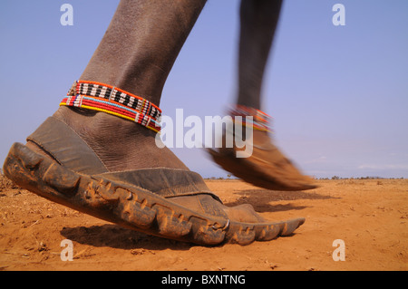 Un guerrier Masaï marche à travers le paysage aride et poussiéreux portant son chaussures en caoutchouc, unique, faite de vieux pneus. Banque D'Images