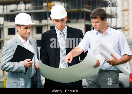 Portrait de trois constructeurs au chantier permanent et de discuter de nouveau projet, un des hommes Banque D'Images