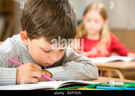 Photo de clever schoolkid écrit quelque chose dans son cahier de leçon sur l'arrière-plan de camarade Banque D'Images