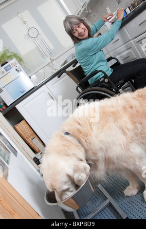 Femme handicapée en fauteuil roulant dans une cuisine avec son chien Banque D'Images