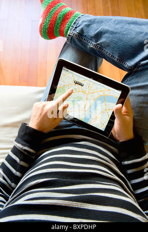 L'homme à la maison à l'aide d'un Apple iPad pour regarder Google maps sur ses genoux. Banque D'Images