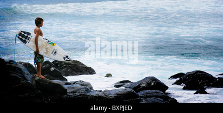 Un jeune surfer regardant le spot de surf sur les rochers au parc de Hookipa Maui sur l'Îles Hawaïen Banque D'Images