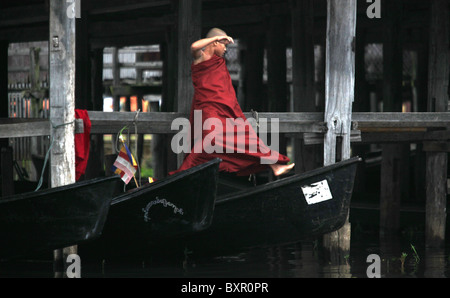 Un moine novice saute entre les bateaux à un monastère flottant sur le lac Inle situé dans la collines Shan au Myanmar (Birmanie). Banque D'Images