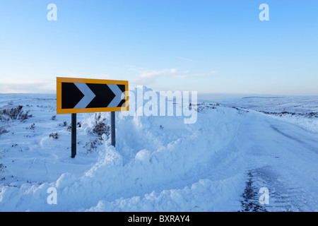 Chevron panneau d'avertissement sur un coude recouvert de neige qui a été labouré neige montrant dangers de la conduite en hiver Banque D'Images