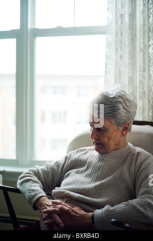 Vieille Femme assise dans un fauteuil avec les mains jointes. Banque D'Images