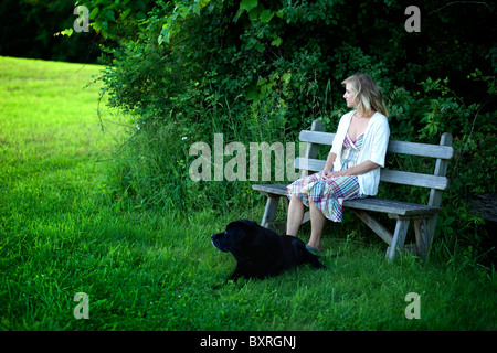 Femme assise sur un banc de travail avec chien labrador noir à côté Banque D'Images