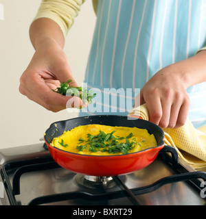 Ajouter les herbes hachées pour garçon omelette dans poêle Banque D'Images