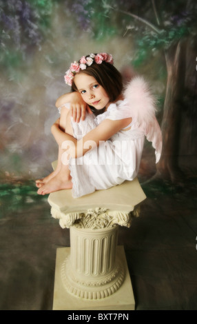 Belle jeune fille portant des ailes d'ange rose et fleurs halo assis sur un piédestal Banque D'Images