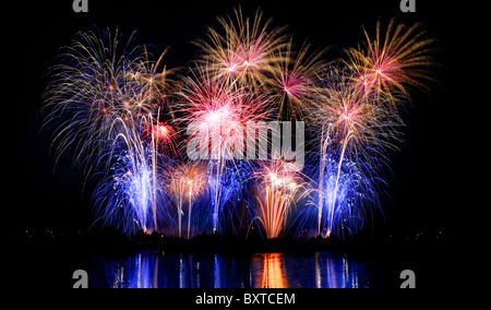 Une nuit de l'heure d'artifice aérienne colorée reflétée dans l'eau. Banque D'Images