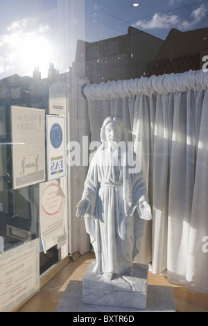 Une petite statuette de Jésus se tient en plein soleil dans un funérarium's fenêtre avant. Banque D'Images