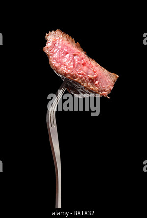 Un morceau de steak grillé sur une fourchette, isolé sur le noir. Banque D'Images
