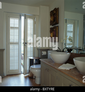 Louvre Plantation volets sur des portes françaises dans la salle de bains moderne blanc avec double vasque vasques sur meuble recouvert de marbre Banque D'Images