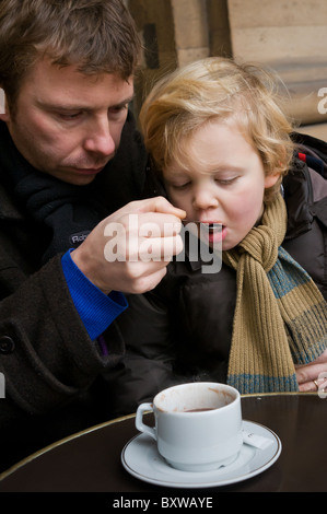 Père et son fils, profiter d'un chocolat chaud à l'extérieur d'un café de Paris en hiver. Banque D'Images