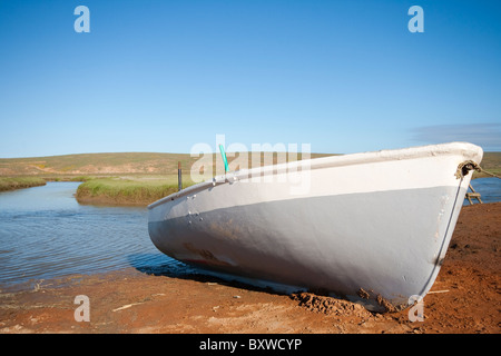 Un petit bateau de pêche en fibre de verre est situé sur la rive de la rivière en arrière-plan et bleu ciel Banque D'Images