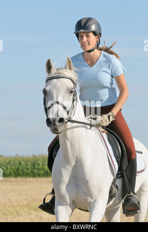 Jeune cavalier au dos d'un poney allemand blanc galoper dans un champ de chaume Banque D'Images