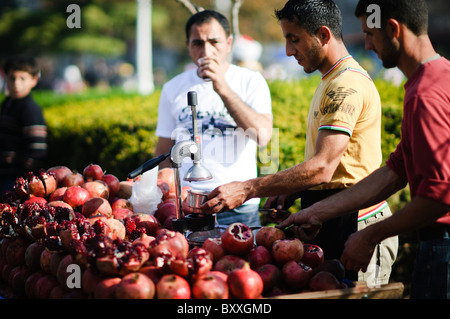 ISTANBUL, Turquie / Türkiye — Un vendeur ambulant utilise une centrifugeuse à grenade traditionnelle pour préparer des jus de fruits frais dans les rues animées d'Istanbul. Cette scène vibrante est un spectacle commun dans la ville, reflétant la riche culture culinaire d'Istanbul et la vie de rue animée. Le jus de grenade fraîchement pressé est un rafraîchissement populaire parmi les habitants et les touristes. Banque D'Images