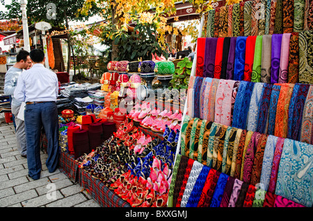 Stall souvenir des écharpes en soie Istanbul Turquie // ISTANBUL, Turquie — Un stand vendant des écharpes en soie et d'autres souvenirs dans les rues d'Istanbul près de Sainte-Sophie. L'exposition vibrante comprend des foulards colorés à motifs, des pantoufles turques traditionnelles et des articles décoratifs, attirant les passants. Banque D'Images