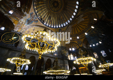 ISTANBUL, Turquie — le vaste hall principal de la basilique Sainte-Sophie présente son remarquable design architectural byzantin, avec son massif dôme central soutenu par des pendentifs et des semi-dômes. L'intérieur présente à la fois des éléments chrétiens et islamiques, y compris des mosaïques byzantines, de la calligraphie ottomane et de grands avize ottomans (lustres). D'énormes colonnes et panneaux de marbre bordent l'espace, démontrant la grandeur de l'ingénierie architecturale du vie siècle. Banque D'Images