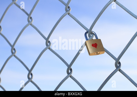 Cadenas verrouillé avec coeur suspendu à une chaîne barrière avec un ciel bleu en arrière-plan. Banque D'Images