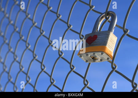 Cadenas verrouillé avec coeur suspendu à une chaîne barrière avec un ciel bleu en arrière-plan. Banque D'Images