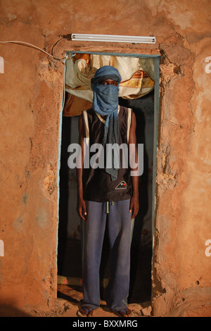 Un jeune homme Peul dans le turban se tient dans l'encadrement de la porte de sa maison à Djibo, le nord du Burkina Faso. Banque D'Images