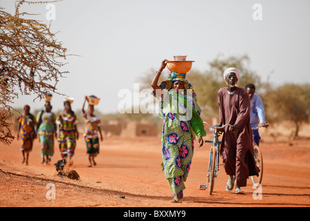 Les femmes arrivent dans la ville de Djibo, au Burkina Faso, à pied, transportant leurs marchandises sur leurs têtes à la mode traditionnelle africaine. Banque D'Images