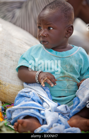 Dans la ville de Djibo, au nord du Burkina Faso, un enfant joue tranquillement que sa mère vend des verts sur le marché. Banque D'Images