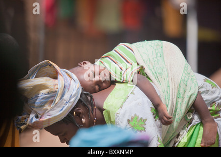 Dans la ville de Djibo, au nord du Burkina Faso, une femme se penche pour examiner le gombo dans le marché, bébé au dos. Banque D'Images